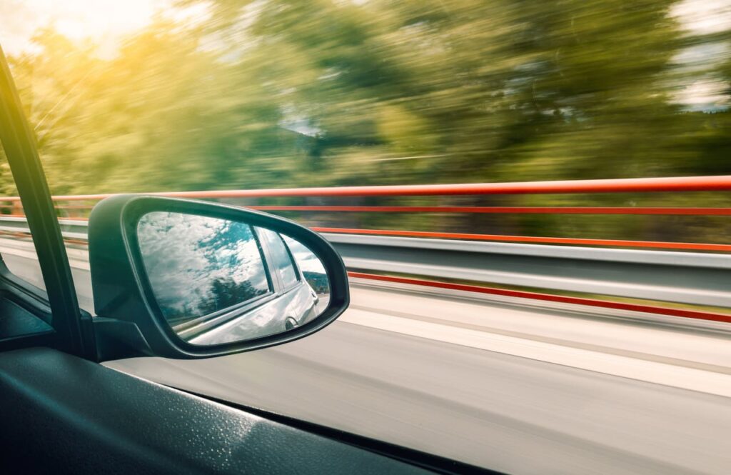 Side mirror view capturing high-speed travel on an expressway with motion blur effect.